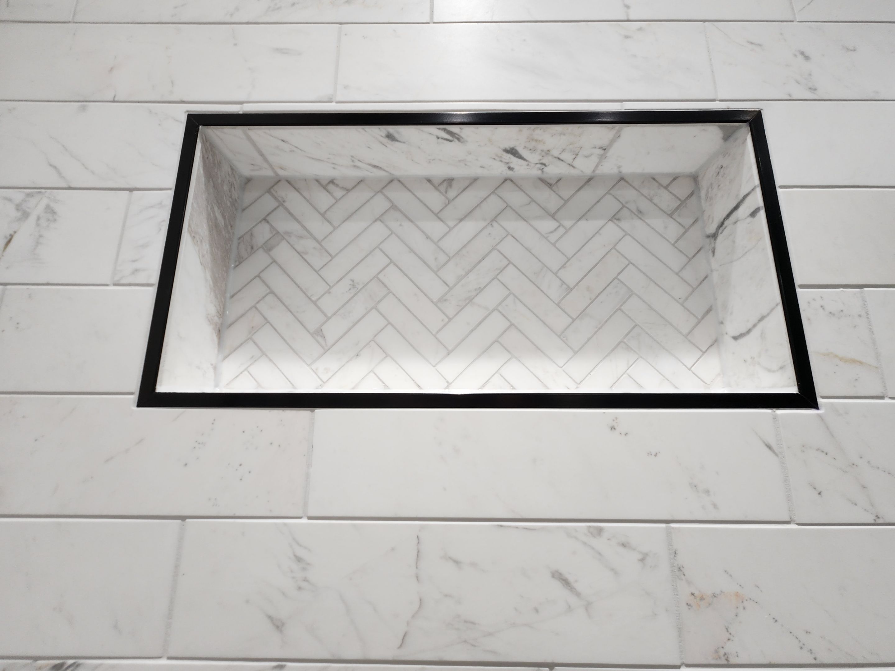 built in shower shelf with marble tile, black frame, and chevron shower tiles