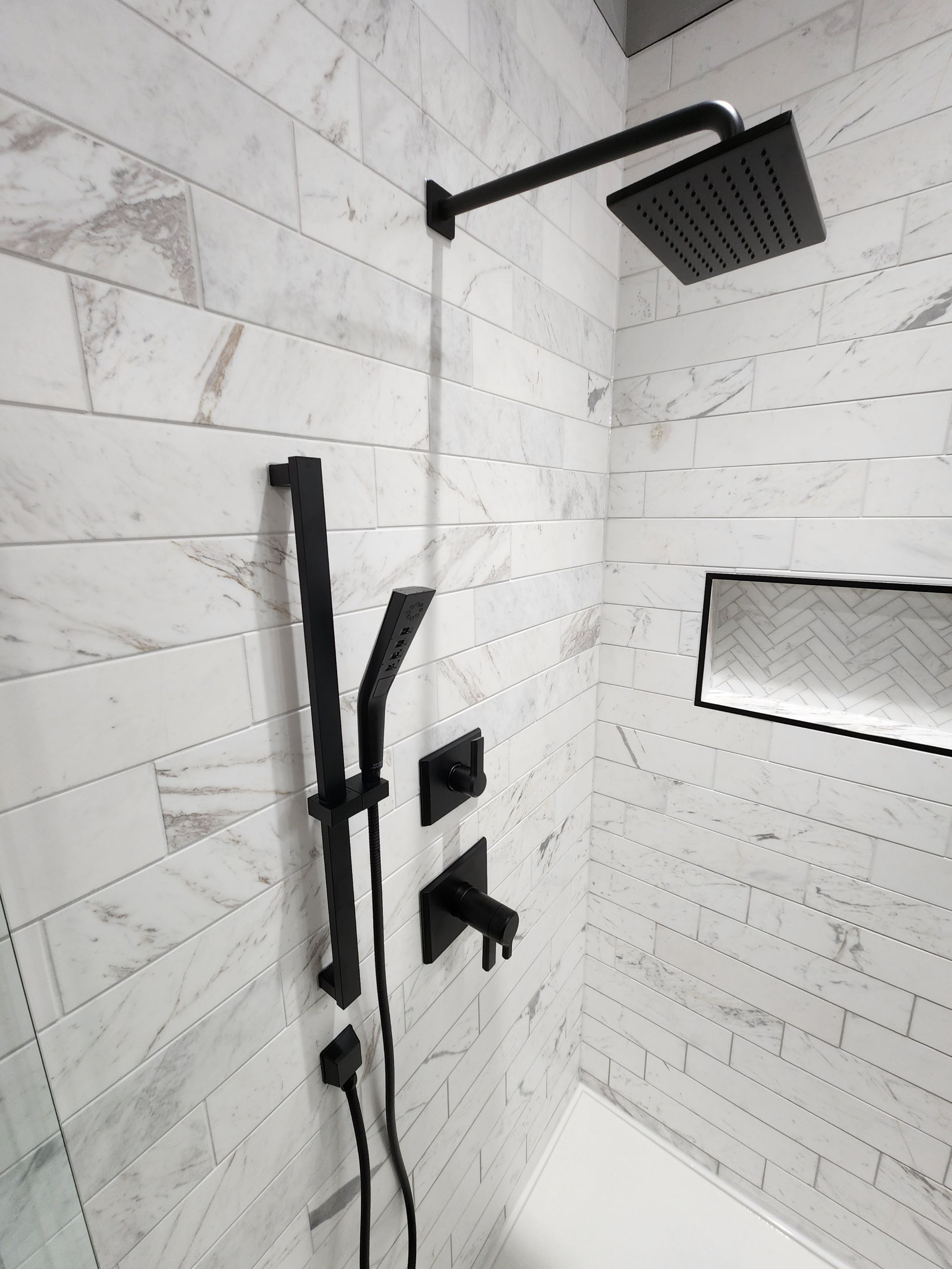 modern shower in a san antonio bathroom remodel with black shower head, built in shower shelf, and marble tiles