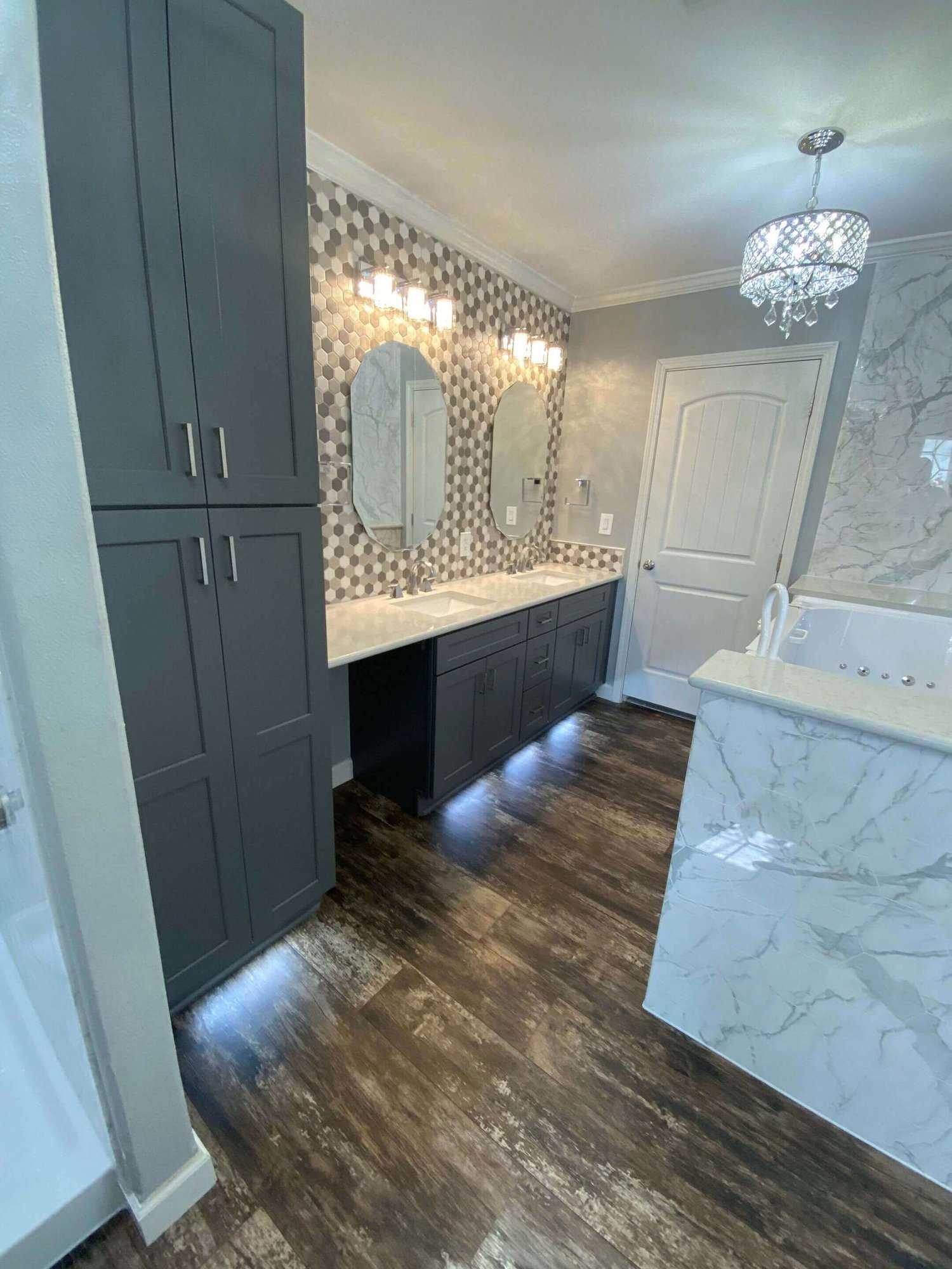 A modern bathroom featuring dark wood-look flooring, grey cabinetry with silver handles, and a double vanity with two oval mirrors.